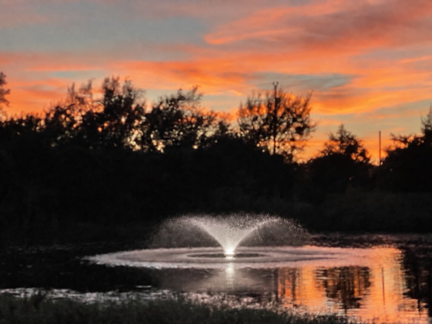 The Red Door Ranch pond fountain glowing white beneath a colorful sunset